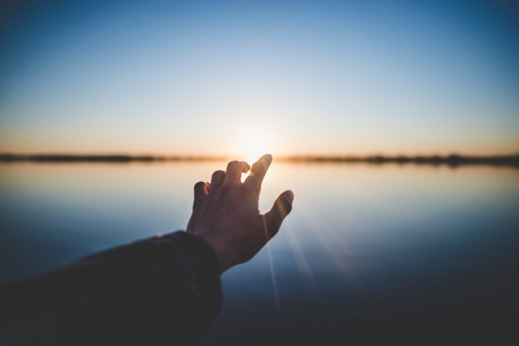 Hand reaching towards the horizon over water.